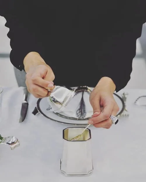 A jeweler meticulously resetting a diamond into a new platinum ring, with various tools and different settings on a velvet tray beside them.