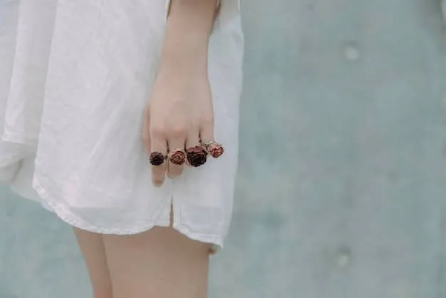 A close-up of a woman's hands adorned with multiple rings of various sizes and styles, showcasing a mix of metals and stones, with a minimalist background.