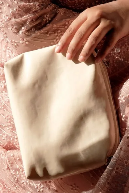 A close-up of a person's hand artfully tying a patterned silk scarf around the handle of a minimalist white handbag, demonstrating a simple repurposing technique.