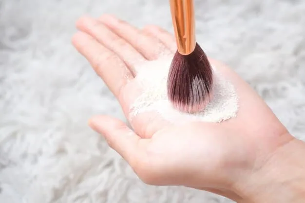 A close-up of a hand holding a fluffy powder brush applying translucent powder to a face.