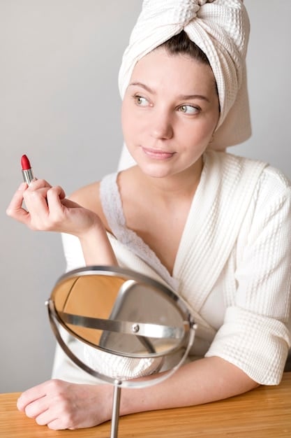 A woman subtly dabbing her lips with a tissue, with a small tube of lipstick and a compact mirror on a table in front of her, conveying a natural touch-up moment.