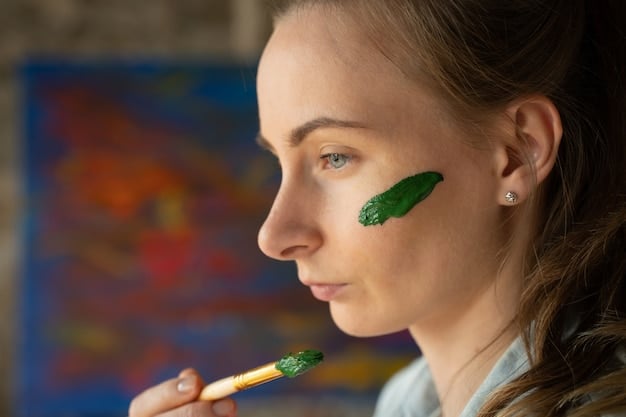 A makeup artist's hand delicately applying a green color corrector stick to a model's cheek, targeting a small area of redness. The application is precise and minimal.