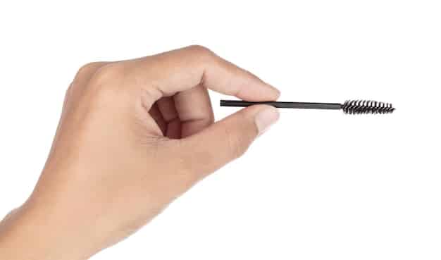 A person's hand holding a lash applicator, precisely placing a false eyelash onto a clean, prepped eyelid.