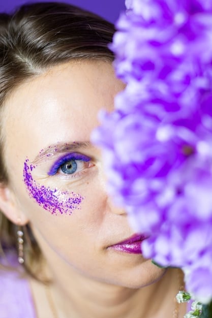A close-up of an eye showcasing a vibrant purple smoky eye with subtle silver glitter on the inner corner, highlighting a bold and creative makeup choice.