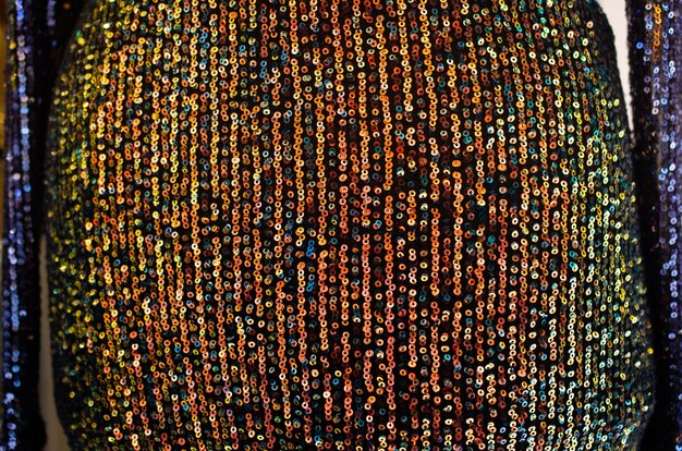 A close-up shot of elaborately beaded and sequined fabric, showcasing intricate patterns and a reflective shimmer under soft lighting. The focus is on the detailed, luxurious texture.