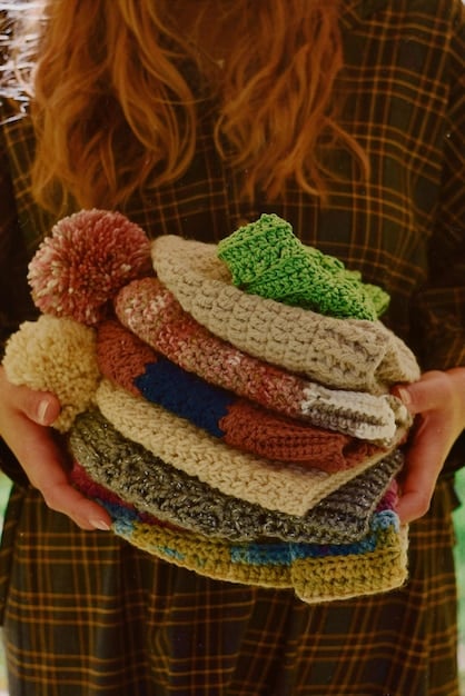 A close-up of hands thoughtfully organizing a meticulously folded stack of sweaters by color, inside a clean wooden drawer. The sweaters are made of soft, high-quality material, and the drawer dividers keep everything perfectly aligned.