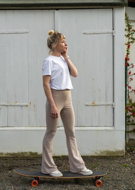 A full-length shot of a woman in a casual spring outfit, featuring a light denim jacket, white t-shirt, and olive green cargo pants, strolling through a vibrant urban street.