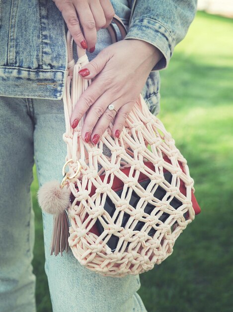 A close-up of a person's hand holding a stylish, oversized woven tote bag in a natural tone, standing in a brightly lit, minimalist entryway, with sunlight emphasizing the bag's texture and modern design.