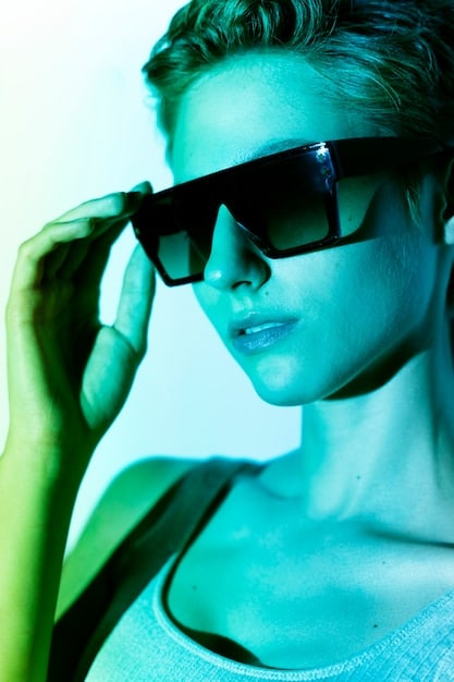 A stylish person wearing large, retro-inspired square sunglasses with a slight tint, complemented by a silk headscarf tied elegantly, standing in front of a blurred urban background, showcasing current eyewear and head accessory trends.